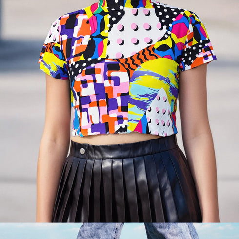 A colorful 90s-style mesh crop top featuring a maximalist abstract pattern. This see-through shirt has a high mock neck, short sleeves, and a vibrant, retro design with geometric shapes, color blocking, and polka dots in bold shades of pink, yellow, blue, and orange. The Y2K-inspired top is a statement piece of festival clothing, perfect for a rave outfit or alternative, dopamine-dressing-inspired streetwear looks.